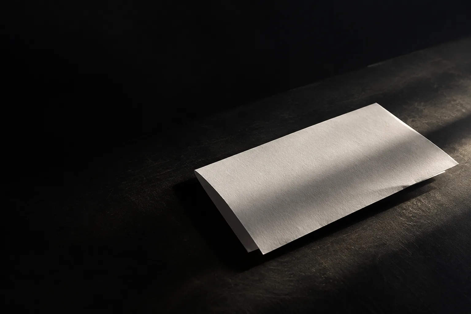 A blank white sheet on a dark surface, lit by a soft beam of light